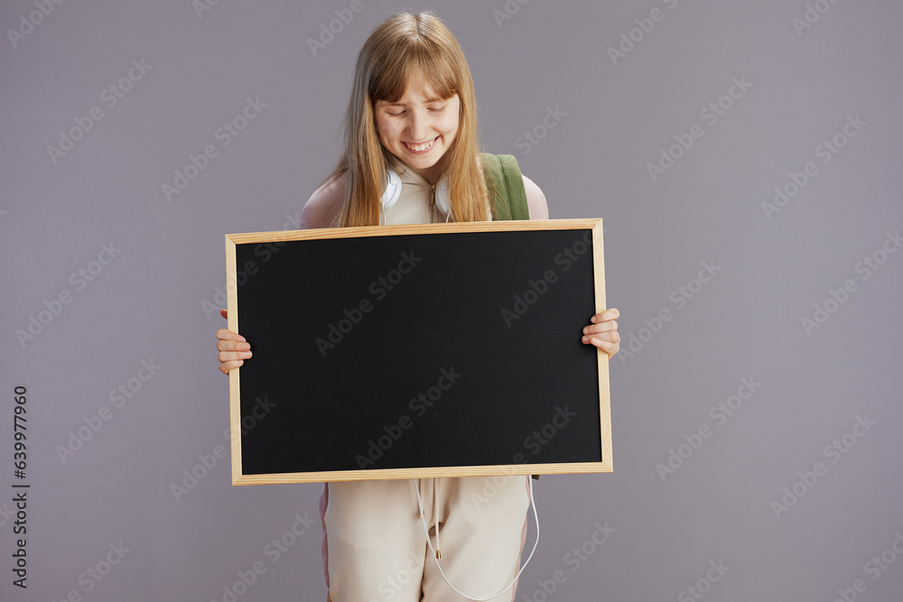 happy trendy pupil in beige tracksuit showing blank board happy trendy pupil in beige tracksuit showing blank board