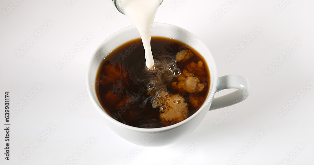 Milk poured into a Cup of Coffee against White Background Milk poured into a Cup of Coffee against White Background