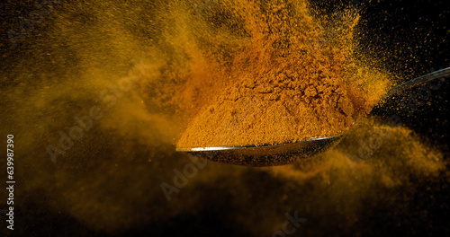 Spoon and Curry Powder falling from Spoon against Black Background