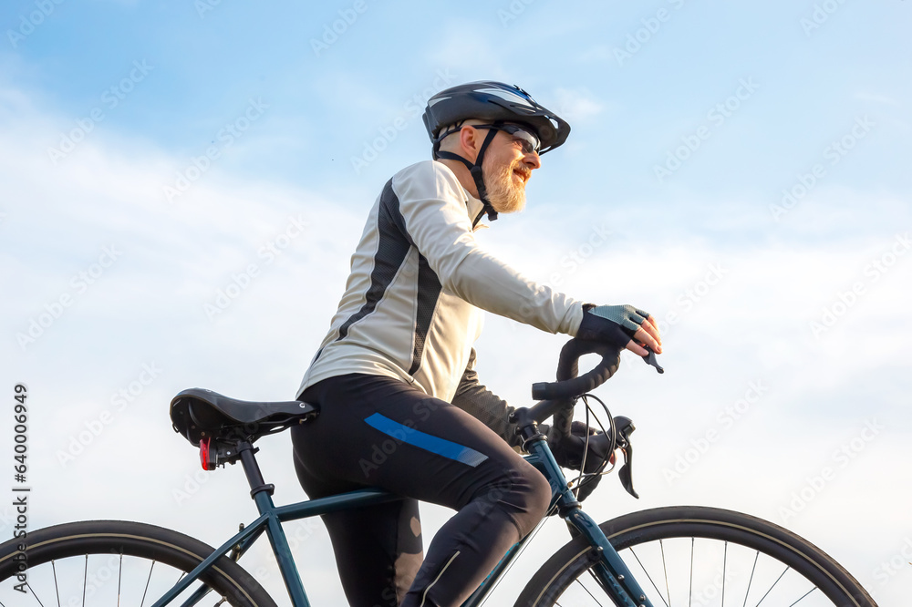 Obraz premium Bearded man cyclist stands with a bike against the blue sky. cycling and health hobbies