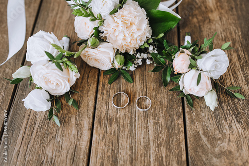 A bouquet of flowers, a boutonniere, golden rings of the newlyweds lie on a wooden background. Wedding photography closeup, top view, concept. © shchus