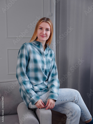 Beautiful woman blonde with natural makeup wear fashion clothes. Female cozy comfort sitting in cozy clean modern living room at home.
