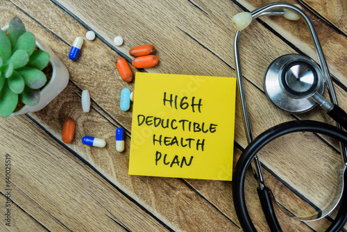 Concept of High Deductible Health Plan write on sticky notes with stethoscope isolated on Wooden Table. photo
