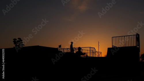 Children during roller skating summer. A view of sporty children silhouettes with roller skates relaxing on sportground durig nightfall time. A concept of active hobby for teens in summer. photo