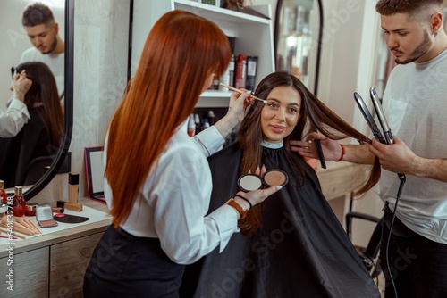 Professional makeup artist and hairstylist preparing female customer in beauty salon. Beauty salon