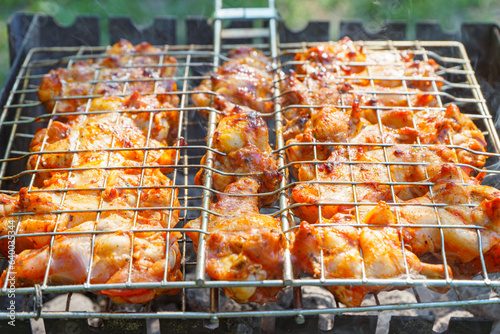 Spicy marinated chicken wings and legs on grill and on a summer barbecue. Cooking process on flame in braizer outside. BBQ, picnic, street food. photo