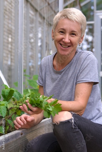 happy woman gardener harvesting greenery at her greenhouse at summer