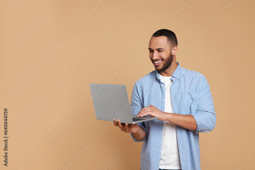Smiling young man with laptop working on beige background, space for text Smiling young man with laptop working on beige background, space for text