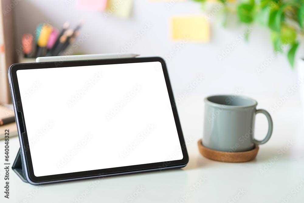 Fototapeta premium Digital tablet with empty screen on coffee cup and notepad on white office desk. Copy space for your text.