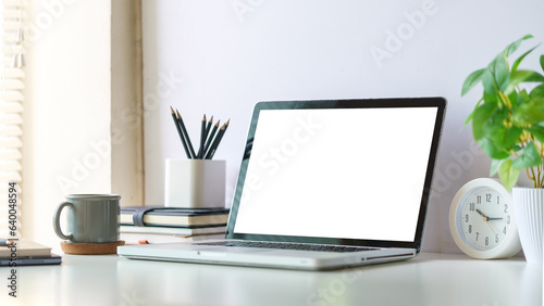 Mock up laptop computer, coffee cup and potted plant on white table. Empty screen for your advertise text. photo