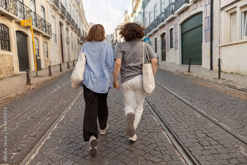 Fototapeta premium Back view of couple in love holding hands while walking on old city street. High quality photo