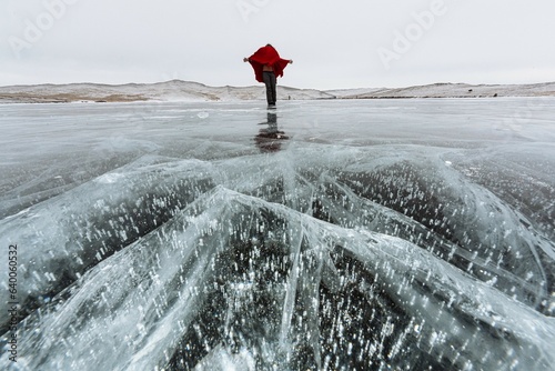 Woman is standing on the ice cracks on frozen Lake Baikal with bank and hills in the background. Selective focus