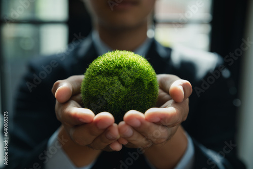 Businessman is holding green globe on hands, ESG and carbon credits ecology concept, carbon neutrality and net zero.