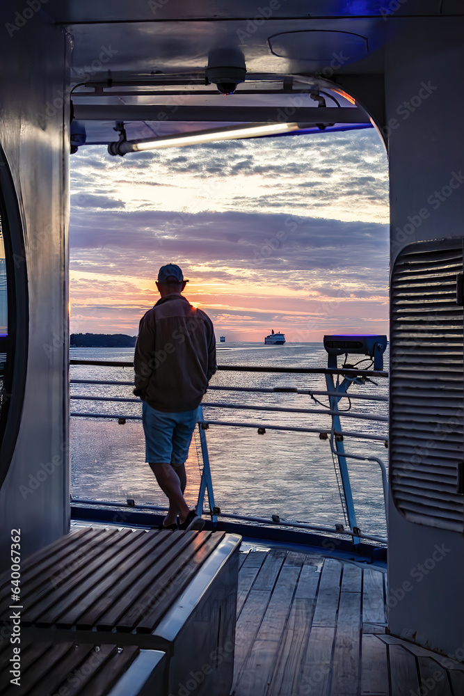 Φωτογραφία Stockholm, Sweden A man on the deck of a ferry from Finland on the Baltic Sea in the Stockholm archiepelago in the rising sun