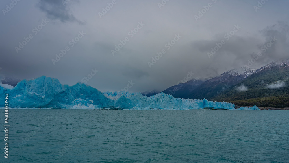 Beautiful glacier Perito Moreno. A wall of blue ice rises above a turquoise lake. Ripples on the water. The surrounding mountains are hidden in clouds and fog. El Calafate. Los Glaciares National Park