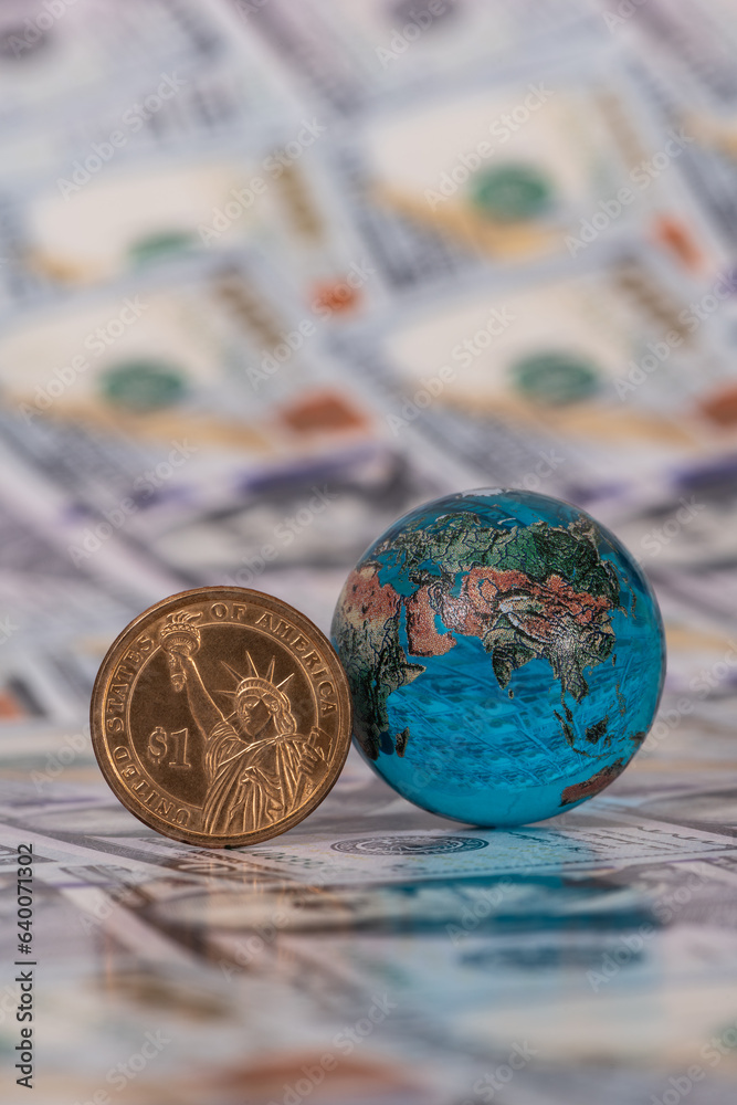 Glass miniature globe and 1 US dollar coin on a flank of 100 US dollar bills Glass miniature globe and 1 US dollar coin on a flank of 100 US dollar bills
