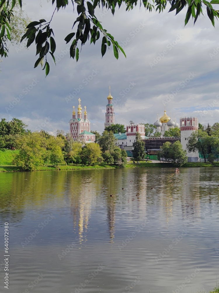 Picturesque view of Novodevichy Monastery on cloudy summer day. Oldest stronghold of Orthodoxy. Mother of God-Smolensk Novodevichy Convent in Moscow. Reflection of buildings on water surface of pond
