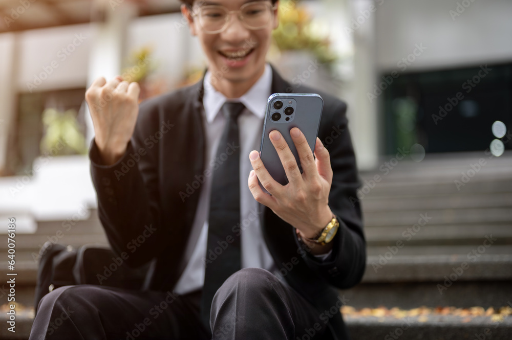 Fototapeta premium Cropped image, A cheerful Asian businessman receiving good news on the phone, got a new job