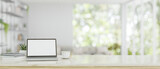 A white-screen laptop mockup on a white tabletop over a blurred, modern bright living room