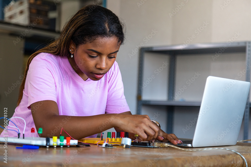 Fototapeta premium Teenage black female high school student in electronics class. African american student using laptop.