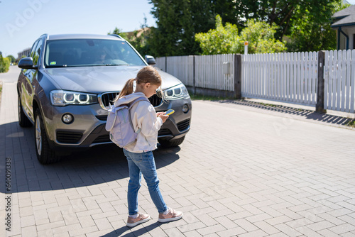 Child looks at a cell phone while crossing a road in front of the car. Concept of mobile phone addiction.