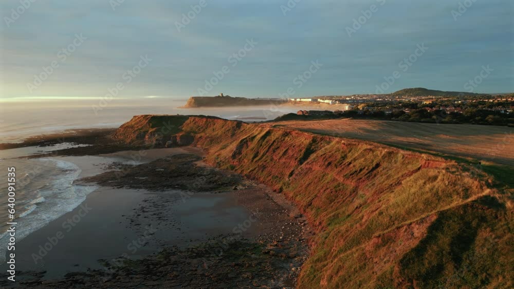 Establishing Aerial Drone Shot of Cleveland Way at Golden Hour at Low Tide with Scarborough Castle in Background Establishing Aerial Drone Shot of Cleveland Way at Golden Hour at Low Tide with Scarborough Castle in Background