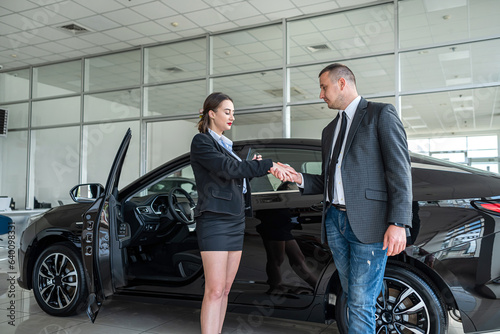 smiling car salesman shakes the hand of a brunette who wants to buy a car. © RomanR