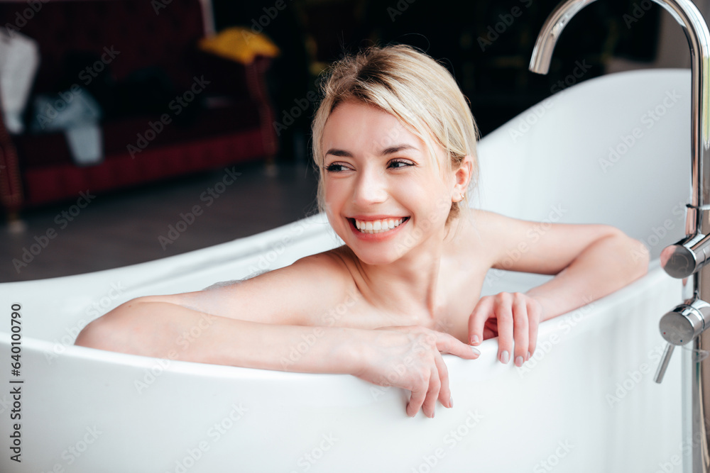Obraz premium Portrait of young beautiful sexy woman having fun while lying in bathtub full of foam at home. Charming smiling model relaxing in luxury bath interior. Female enjoying beauty and skincare day