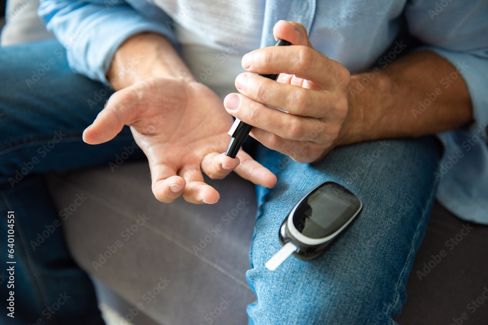 Fototapeta premium Man hands using lancet on finger to check blood sugar or ketones level by glucose meter. Medicine diabetes keto diet health care at home