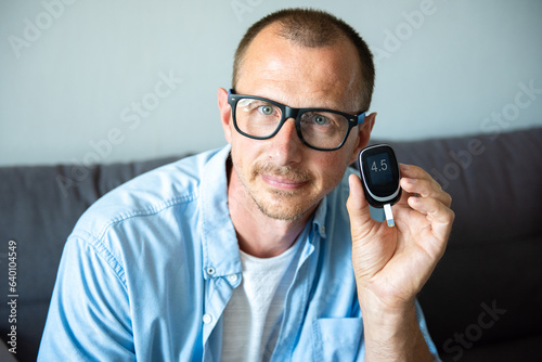 Smiling man holding a blood glucose meter measuring blood sugar. Normal average blood sugar photo