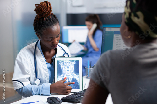 Radiologist showing x-ray ct lung scan explaining clinical information on tablet to patient during appointment. Medic in hospital holding radiology and african american woman at medical checkup. photo