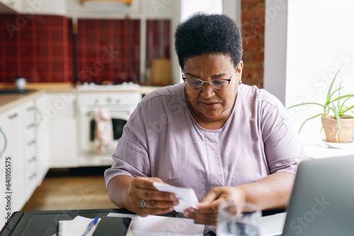 Tablou pe pânză 60-years-old black plus size woman pensioner in glasses reading paycheck for ele