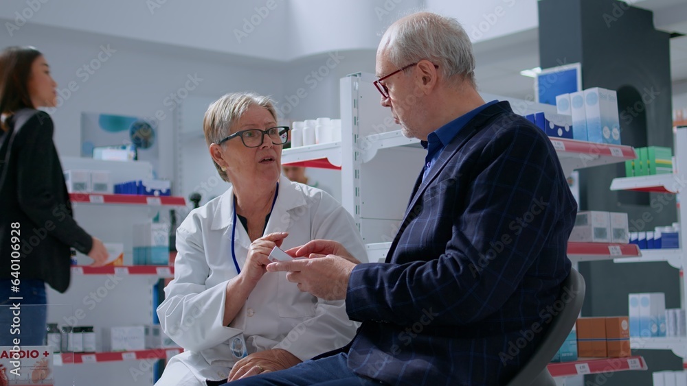 Obraz premium Elderly pharmacist in drugstore with senior patient after finishing annual examination, suggesting him medical products to treat illness symptoms. Older man receiving treatment from specialist