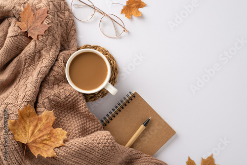 Cozy autumn desk arrangement. Top view featuring snug knitted throw, steaming hot cocoa, spiral notebook, pen, glasses, maple leaves on white backdrop. Add text or ad
