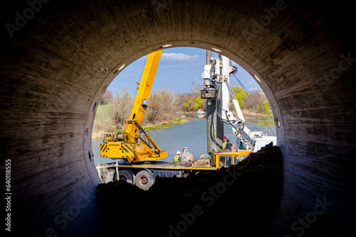 Look through pipe on mobile crane and drilling machine working together on bridge foundation