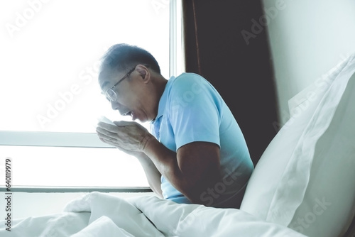 A man who is unwell, sitting in bed at home and blowing his nose into a tissue.