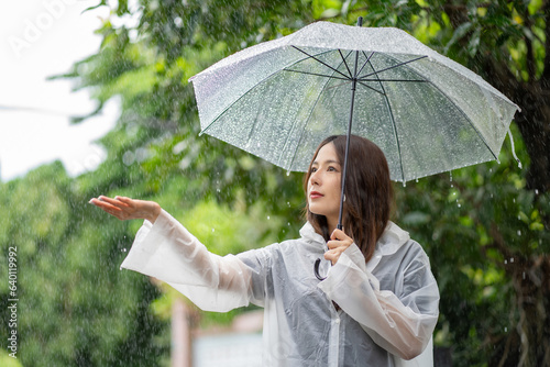 Its raining down hard. Shot of a young asian woman standing in the rain with an umbrella.