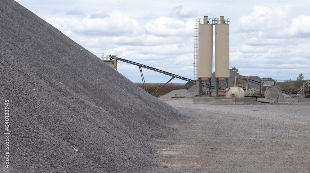 Obraz premium Territory of the asphalt plant. On the territory there is a pile of gravel in close-up against the background of a shipping belt. Clear summer day at the factory.