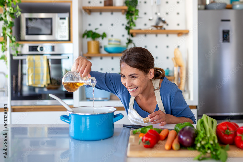 Ecstatic Young Lady Cooking and Sampling Dinner in a Pot, Positioned in a Sleek Kitchen at Home. Home Executive Preparing Wholesome Cuisine with a Grin. Household Management and Nutrient Intake.