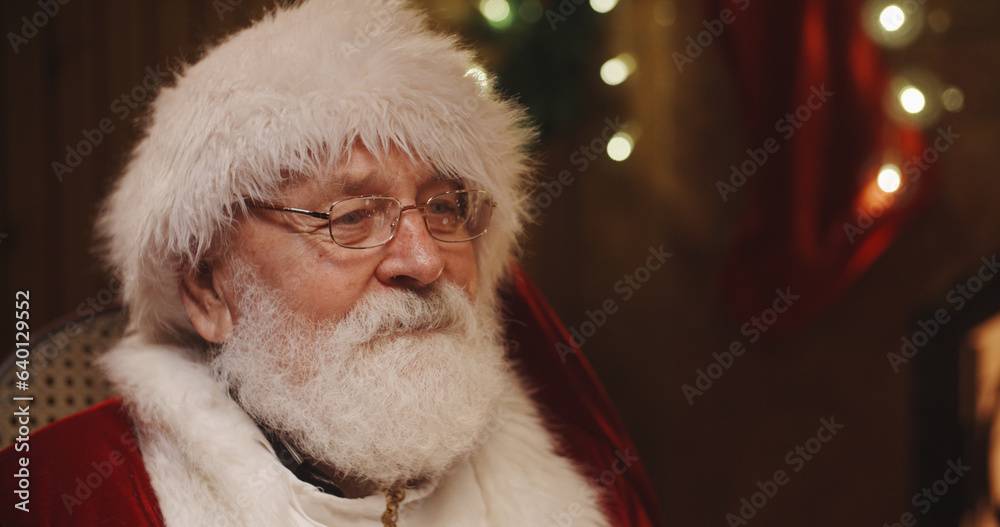 Portrait of happy senior Santa Claus with grey beard and wrinkles on his face, wearing red hat, jacket and white knitted scarf, looking right to the camera Portrait of happy senior Santa Claus with grey beard and wrinkles on his face, wearing red hat, jacket and white knitted scarf, looking right to the camera