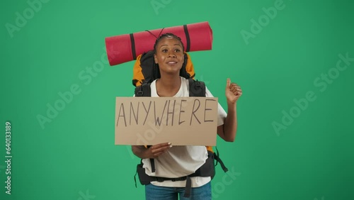 Woman tourist with backpack holding cardboard sign with word anywhere written on it. Isolated on green background. photo