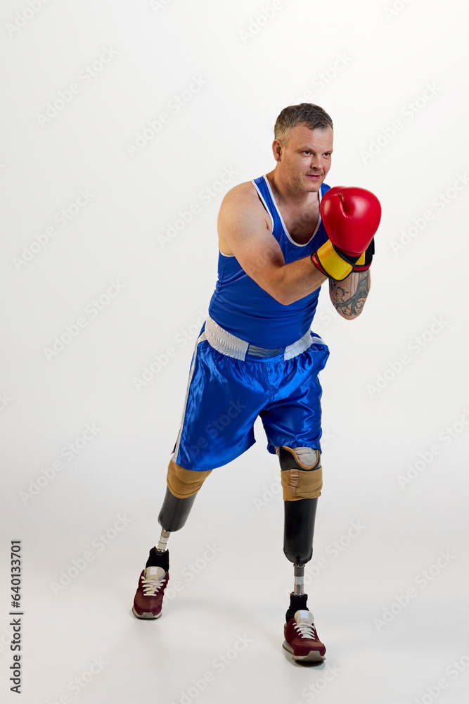 Full length of nice positive man with prosthesis in boxing uniform training indoors and enjoying his hobby against white background.