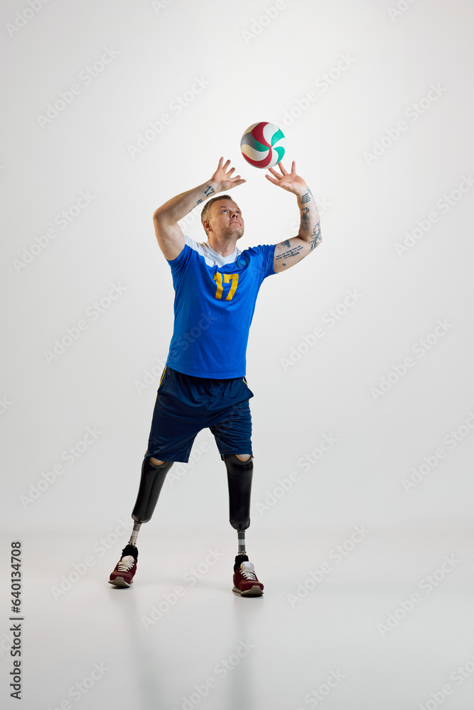 Confident young man with prosthetic legs disability in uniform hits volleyball ball in motion. Inclusive sport for people with disabilities