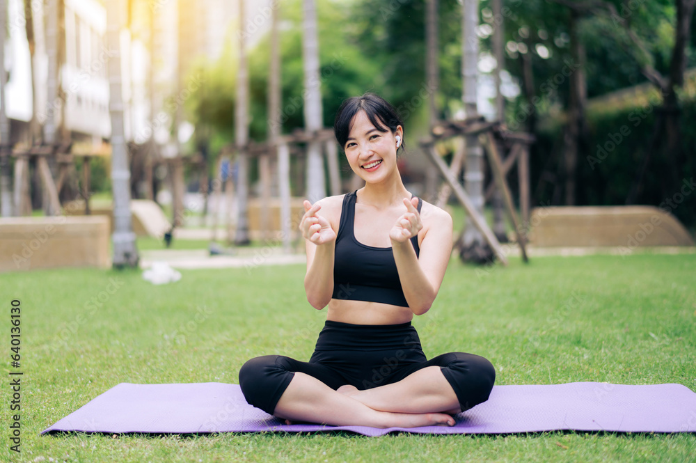Portrait fit pretty young asian woman 30s wearing black sportswear showing mini heart hands gesture on chest while doing yoga and listening relax music in public park. Healthcare wellness concept. Portrait fit pretty young asian woman 30s wearing black sportswear showing mini heart hands gesture on chest while doing yoga and listening relax music in public park. Healthcare wellness concept.