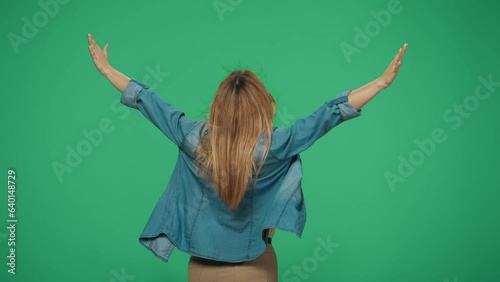 Woman tourist posing with her back at the camera, holding hands up, wind caresses hair. Isolated on green background. photo