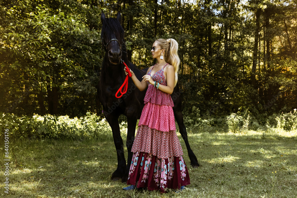 Beautiful blonde woman with a black horse in the ranch. Amazon. Rural girl.