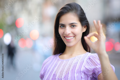 Happy woman gesturing ok standing in the street