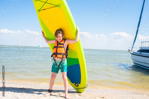 happy 10 year old boy holding a green sup board and paddle for sap boarding on a sunny day at the seaside. 