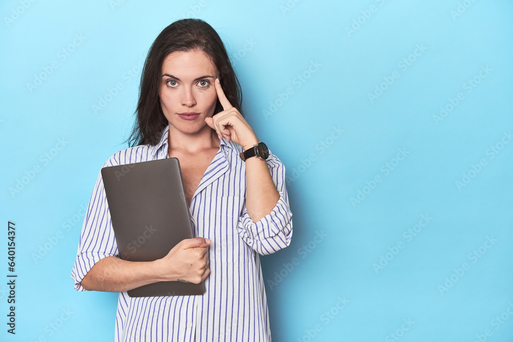 Young businesswoman holding laptop on blue pointing temple with finger, thinking, focused on a task. Young businesswoman holding laptop on blue pointing temple with finger, thinking, focused on a task.