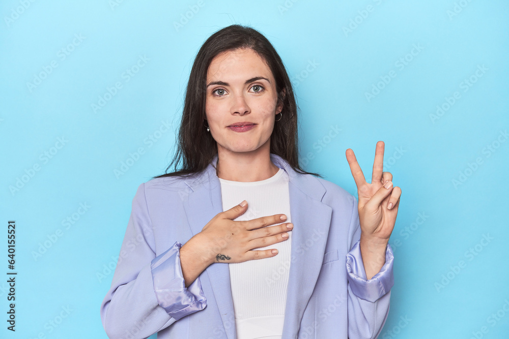 Woman in blue blazer on blue background taking an oath, putting hand on chest. Woman in blue blazer on blue background taking an oath, putting hand on chest.